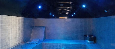 A spa room with a hot tub, tiled walls, and ceiling lights.