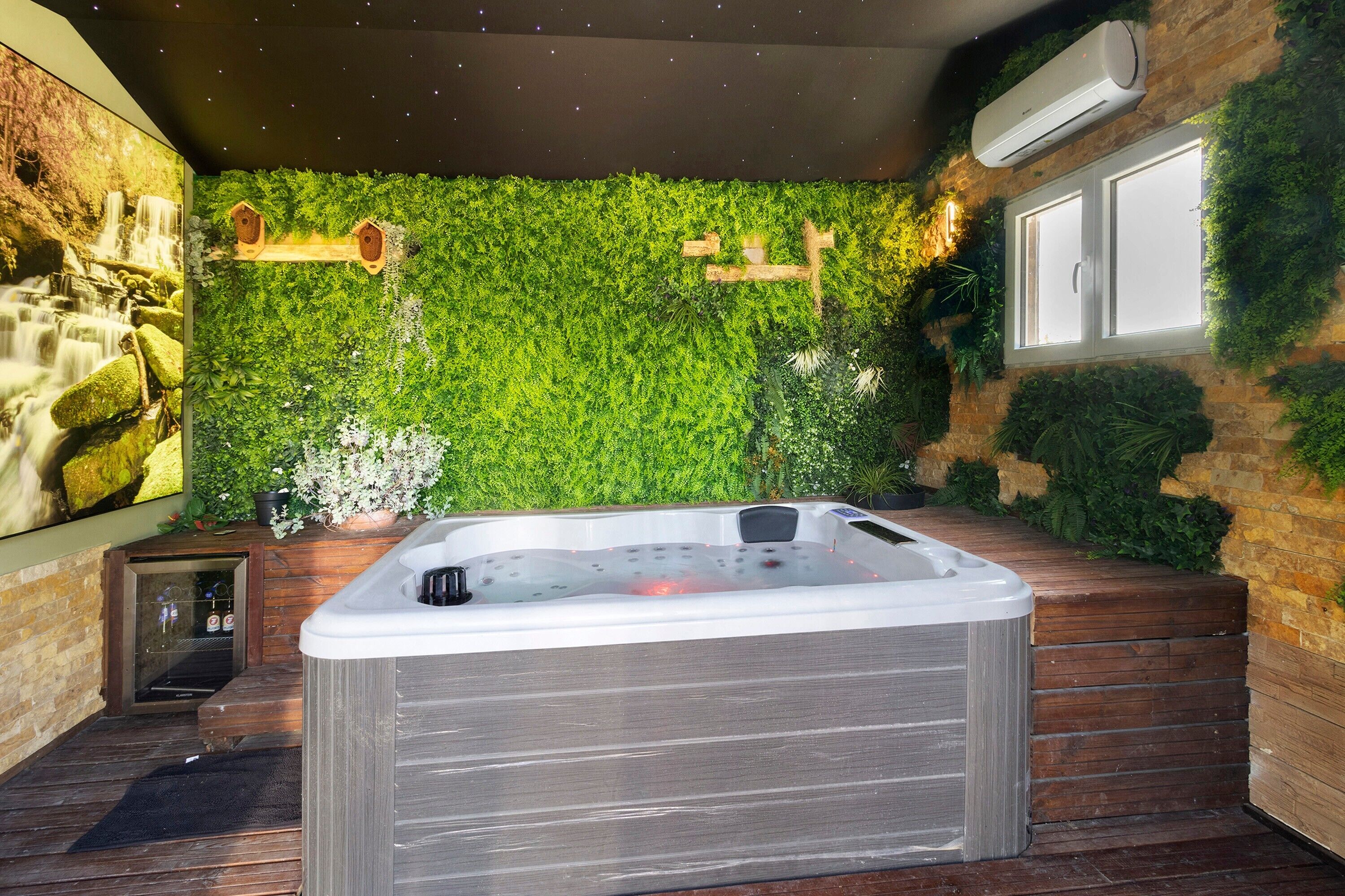 A hot tub in a room with a green wall, wooden flooring, and a window.