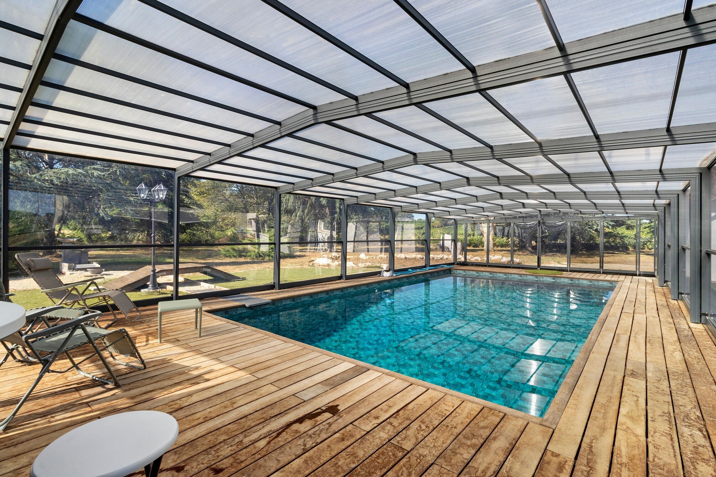 A covered swimming pool with wooden decking and lounge chairs.