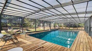 A covered swimming pool with wooden decking and lounge chairs.