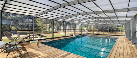 Une piscine couverte dotée d’une terrasse en bois et de chaises longues.