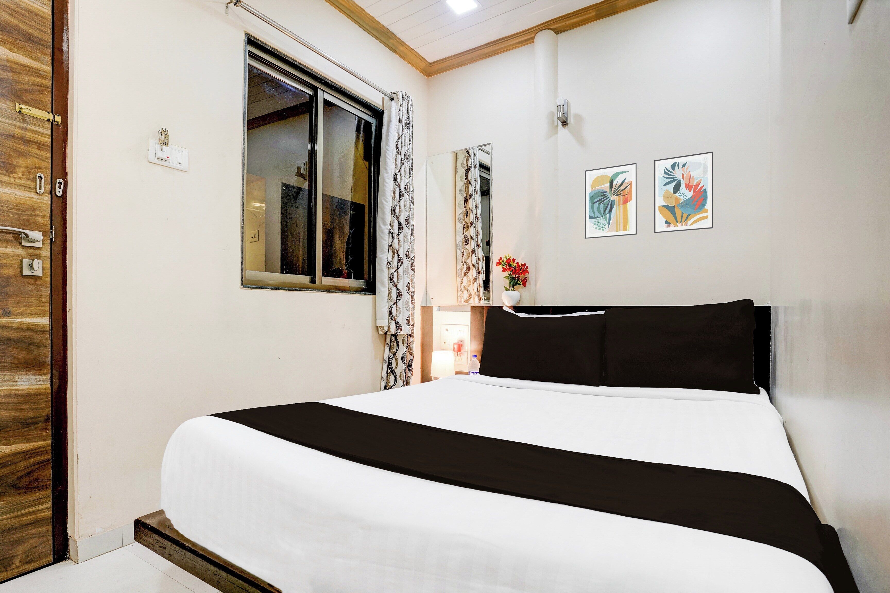Habitación de hotel con cama, ventana, puerta y dos obras de arte colgadas en las paredes.