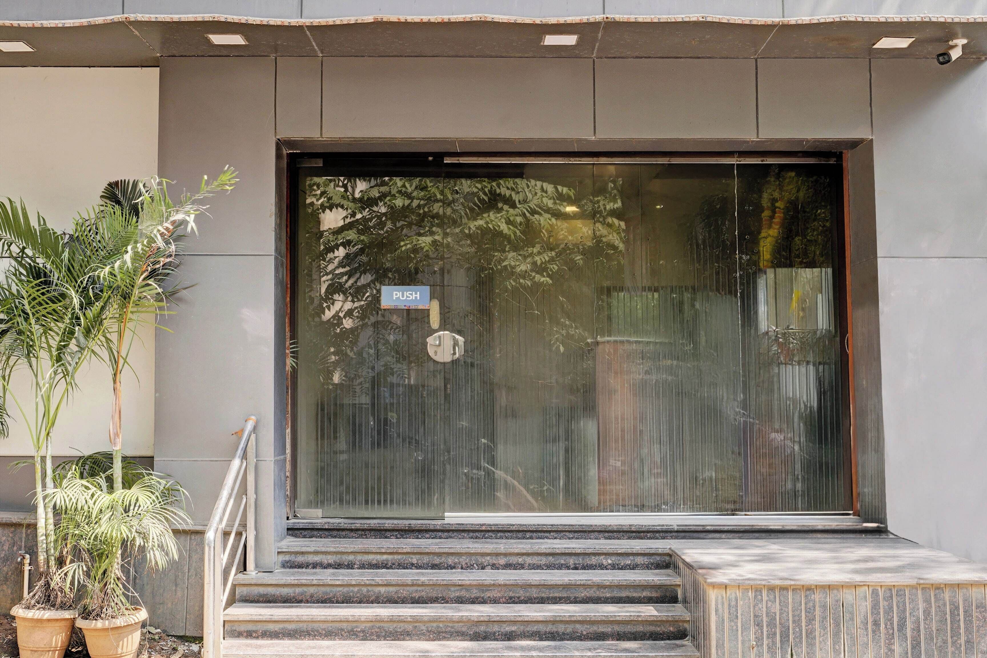 Entrada de un edificio con puerta de vidrio, un botón pulsador y una escalera metálica que sube.