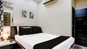 Hotellihuone, jossa on sänky, yöpöytä, lamppu ja seinälle asennettu ilmastointilaite.