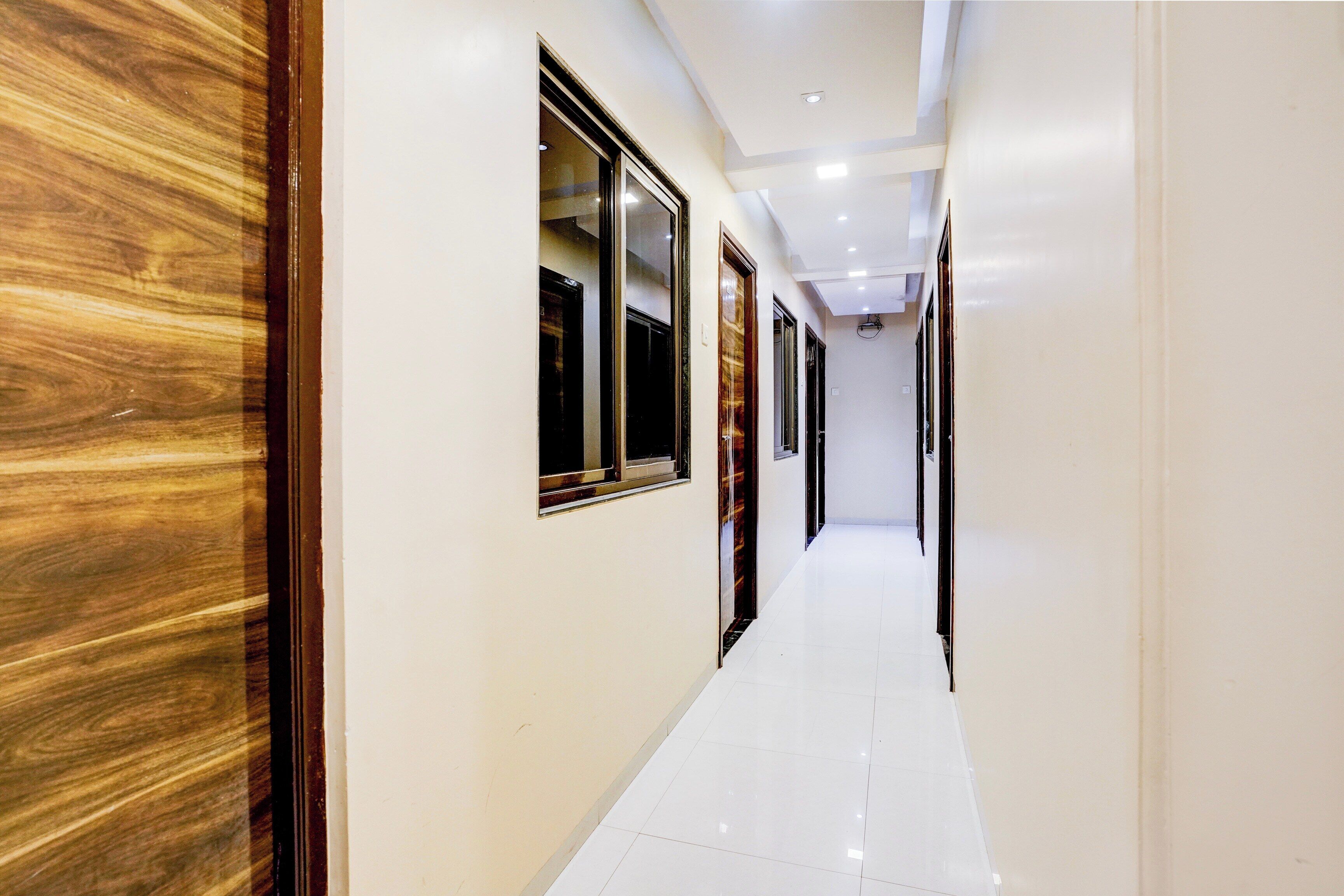 A corridor with doors and windows, leading to a room with a white floor and a wooden wall.