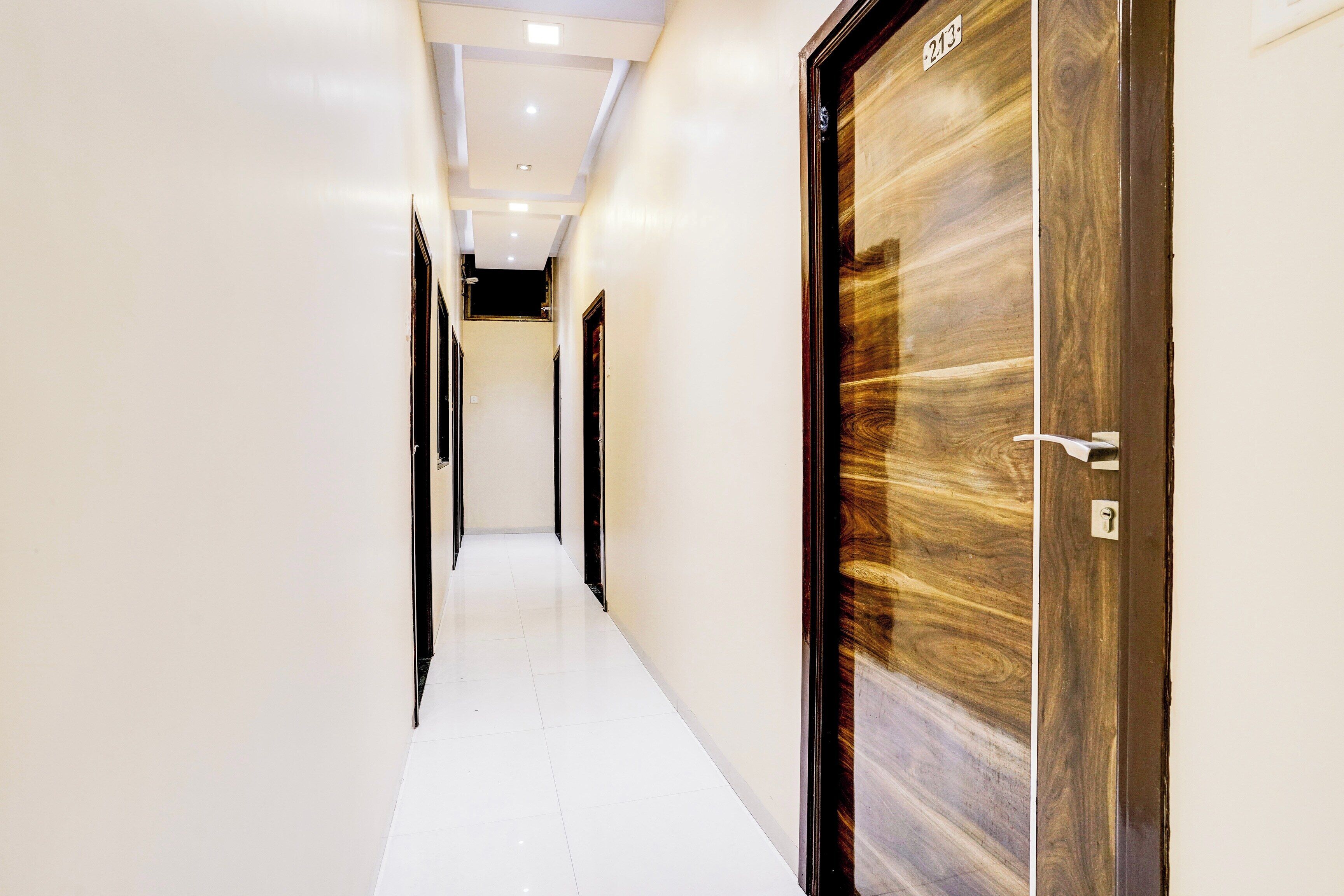 Un pasillo de hotel con puertas a ambos lados, suelo de baldosas e iluminación empotrada en el techo.