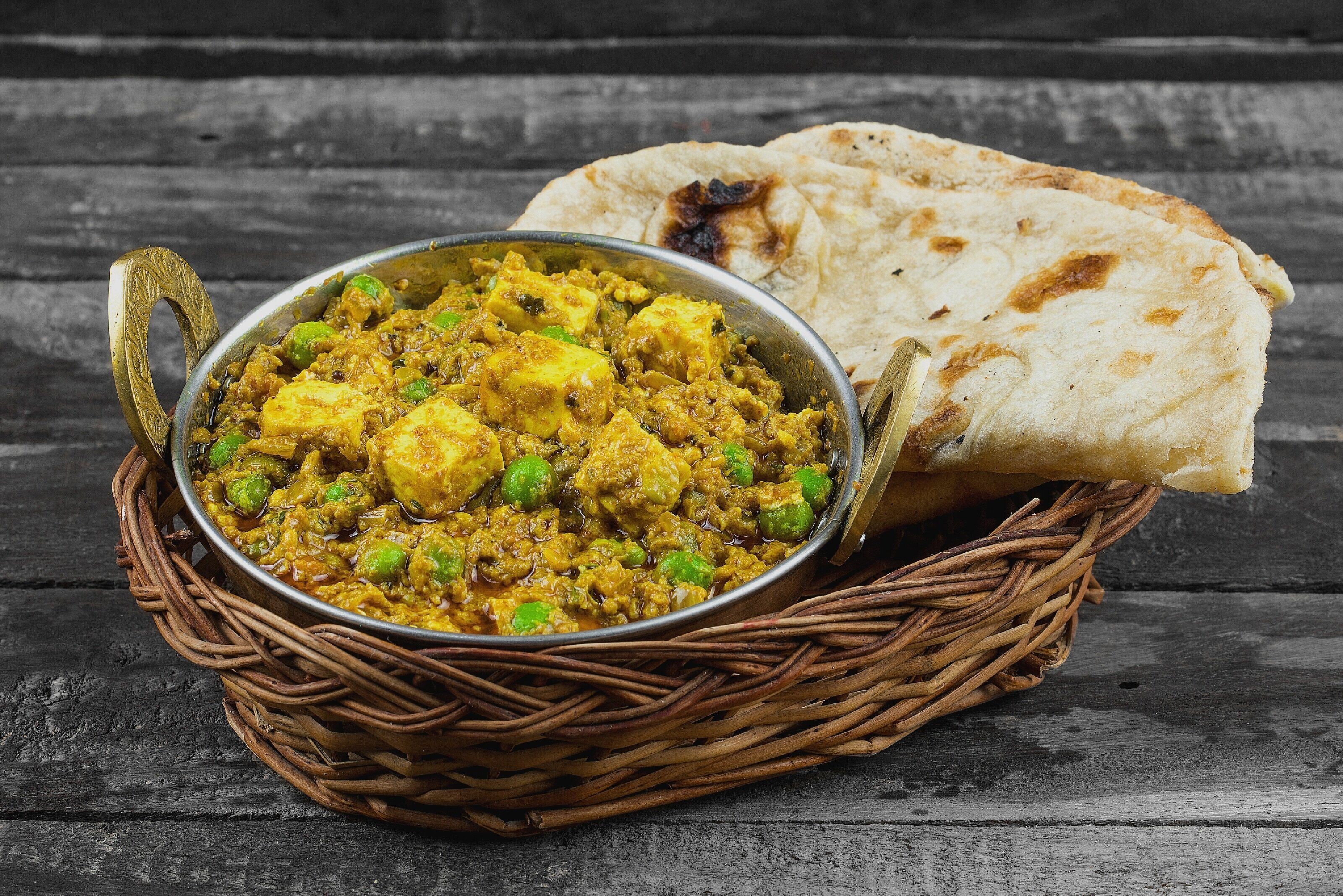 A dish of paneer curry with naan bread on a rustic wooden table.