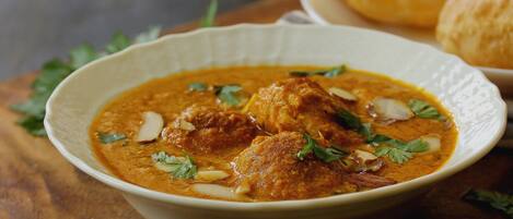 A bowl of curry with meat and potatoes, garnished with herbs, on a wooden table.