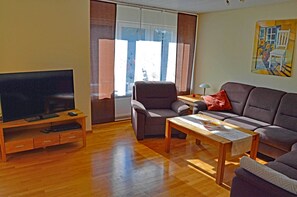 A living room with a flat-screen TV, a sofa, a chair, a coffee table, and a painting on the wall. - Country House Lüneburg Heath – Sleeps up to 6, only 10-min. drive to Heide Park (Neuenkirchen)