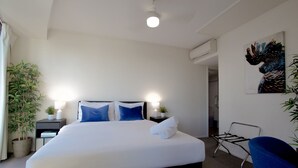 A hotel room with a bed, two bedside tables with lamps, a chair, a potted plant, and a painting on the wall. - Modern Brisbane Studio in the Heart of CBD (Brisbane)