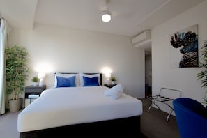 Ein Hotelzimmer mit einem Bett, zwei Nachttischen mit Lampen, einem Sessel, einer Zimmerpflanze und einem Bild an der Wand.