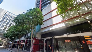 A modern building with a glass facade, trees lining the sidewalk, and storefronts including a Red Bull. - Modern Brisbane Studio in the Heart of CBD (Brisbane)