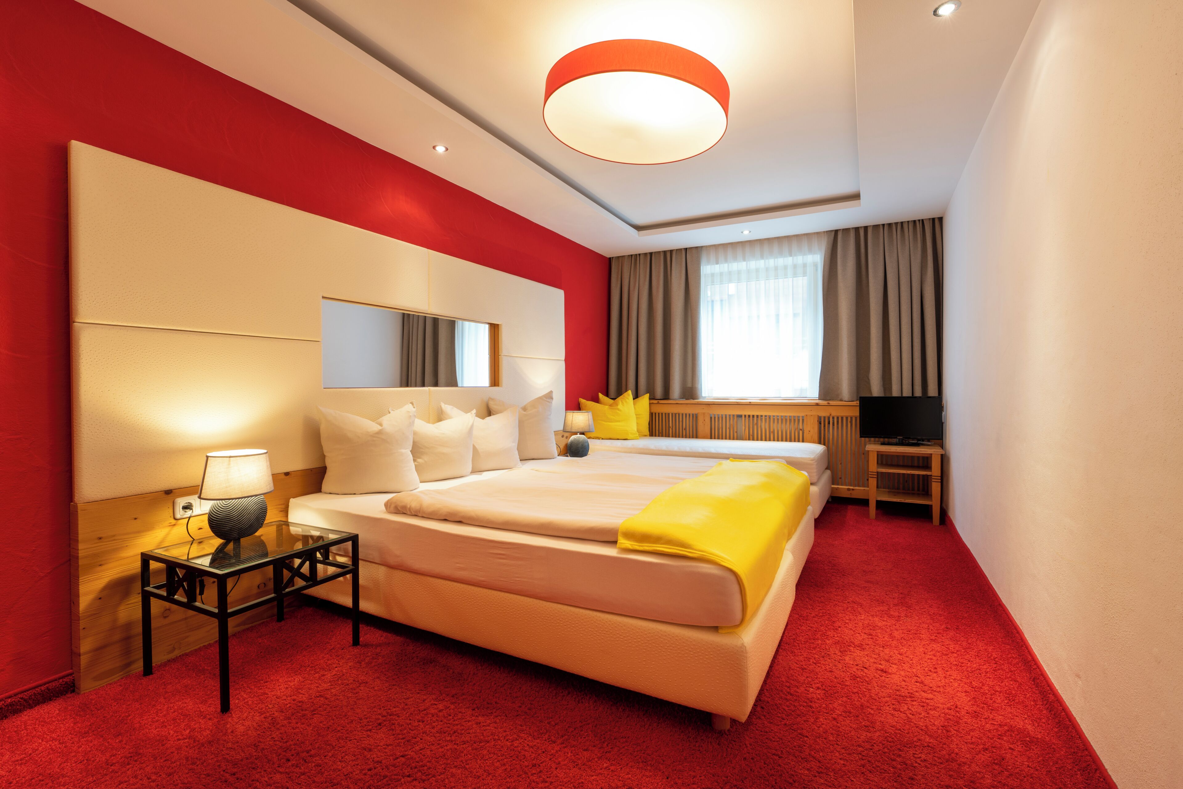 Habitación de hotel con una cama grande, una mesita de noche con lámpara, televisión y ventana con cortinas.