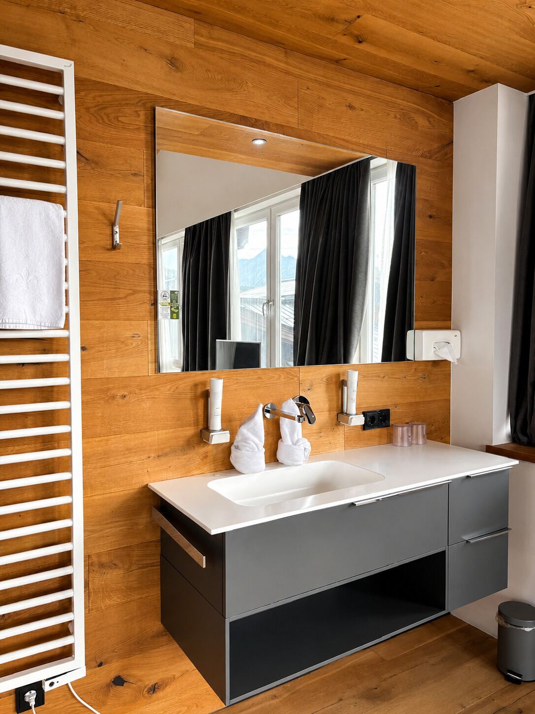 A modern bathroom with a wooden ceiling, a large mirror, a white sink, and a towel rack.