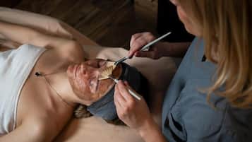 Una persona acostada mientras otra le aplica una máscara facial.