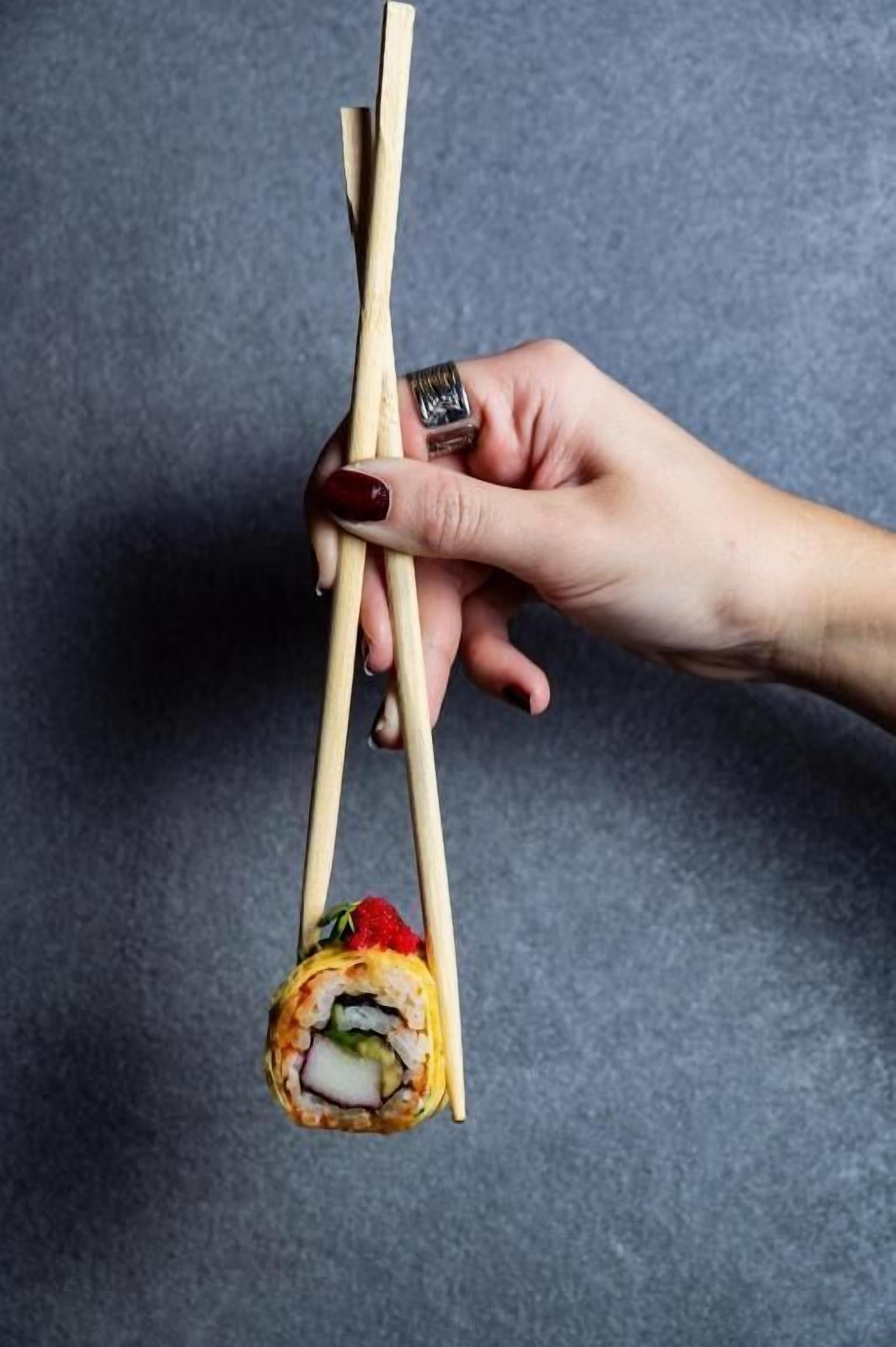 Una mano sosteniendo palillos con un rollo de sushi.