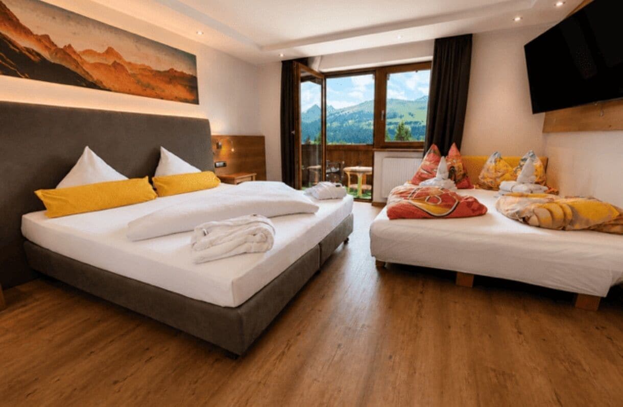 Ein Hotelzimmer mit zwei Betten, einem Bild an der Wand, einem Fernseher und Blick auf die Berge.