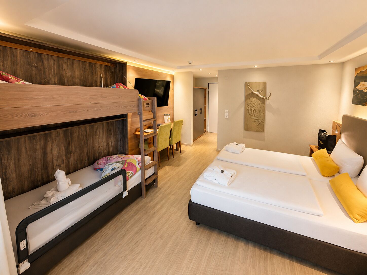 Habitación de hotel con literas, escritorio, cama con almohadas y televisor montado en la pared.