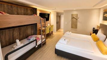 Habitación de hotel con literas, escritorio, cama con almohadas y televisor montado en la pared.