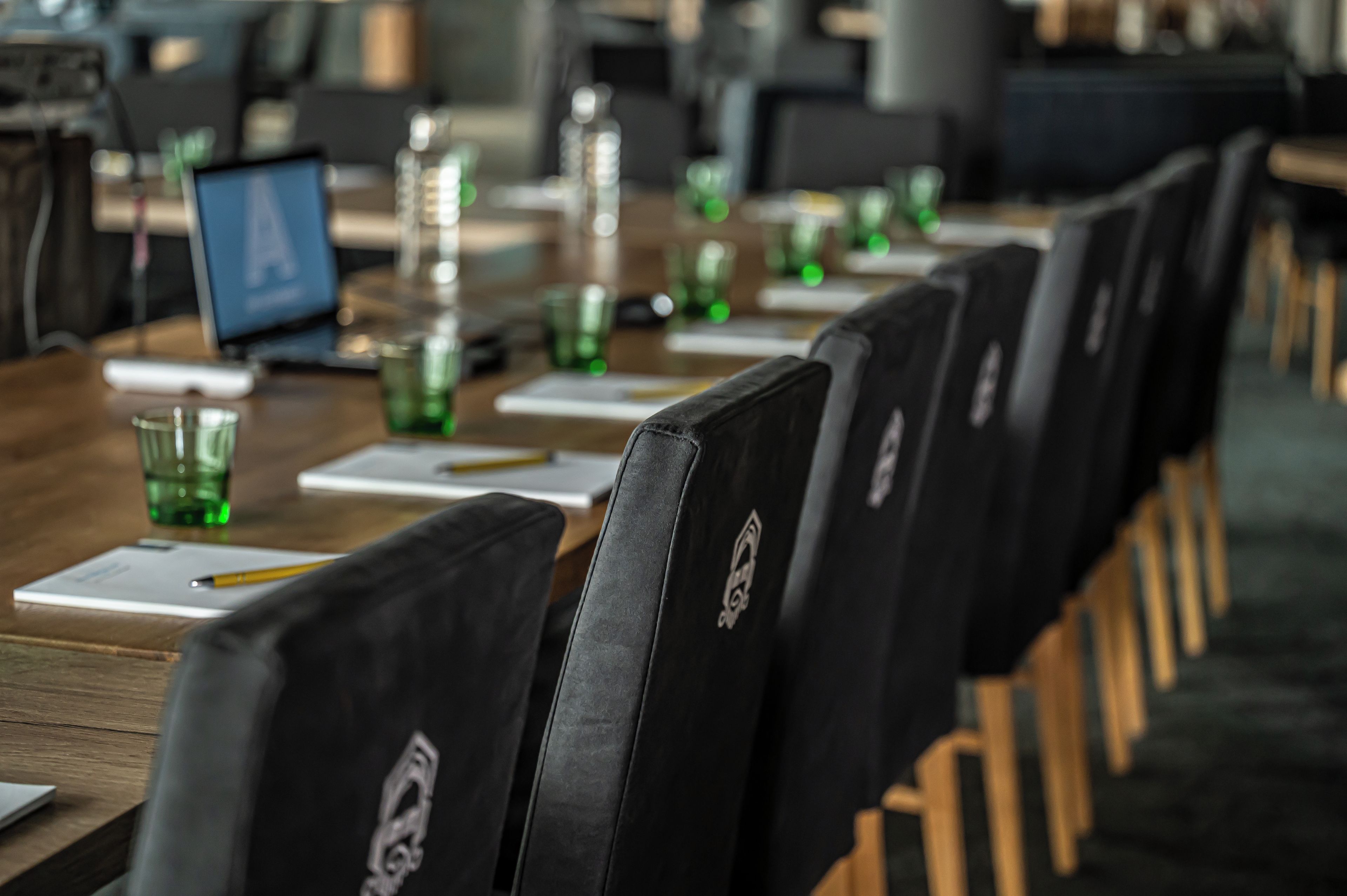 Un salón de conferencias con filas de sillas, una larga mesa con documentos y gafas verdes.