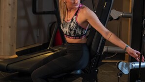 A person using a leg press machine in a gym with a treadmill and a mirror in the background. - MY ALPENWELT Resort – 4 Sterne Superior (Königsleiten)