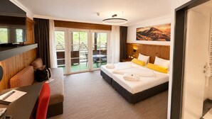 Habitación de hotel con una cama, un escritorio con una silla, un televisor y una puerta corrediza de vidrio que da a un espacio exterior.