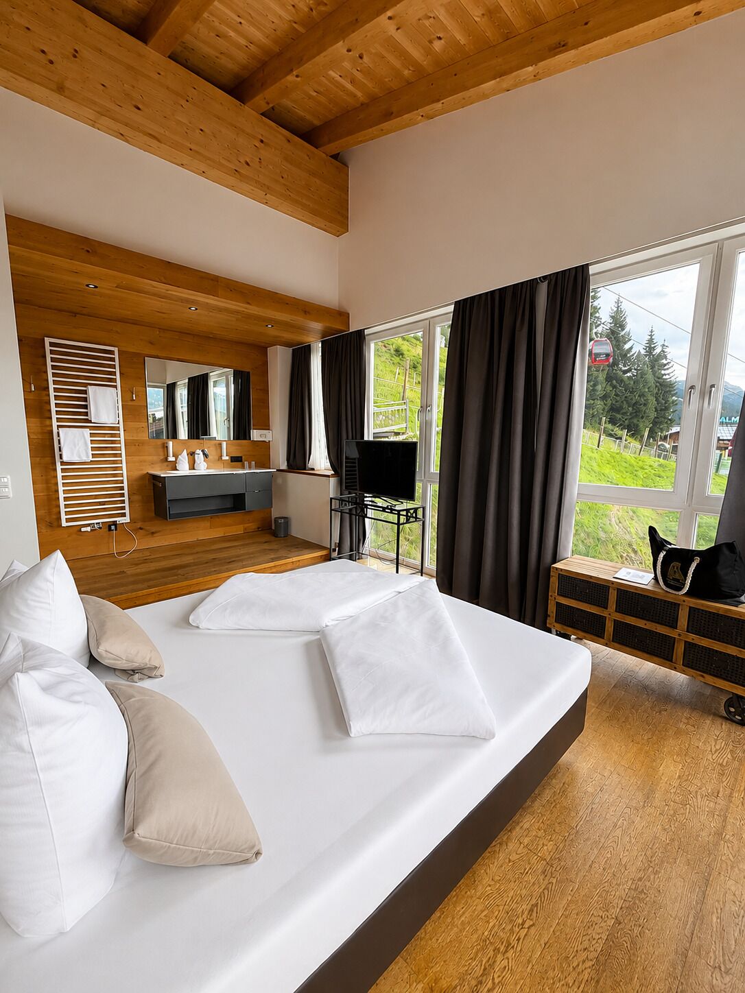 Ein modernes Schlafzimmer mit einem großen Bett, Holzboden, einem Schreibtisch mit Stuhl, einem Spiegel und einem Fenster mit Vorhängen.
