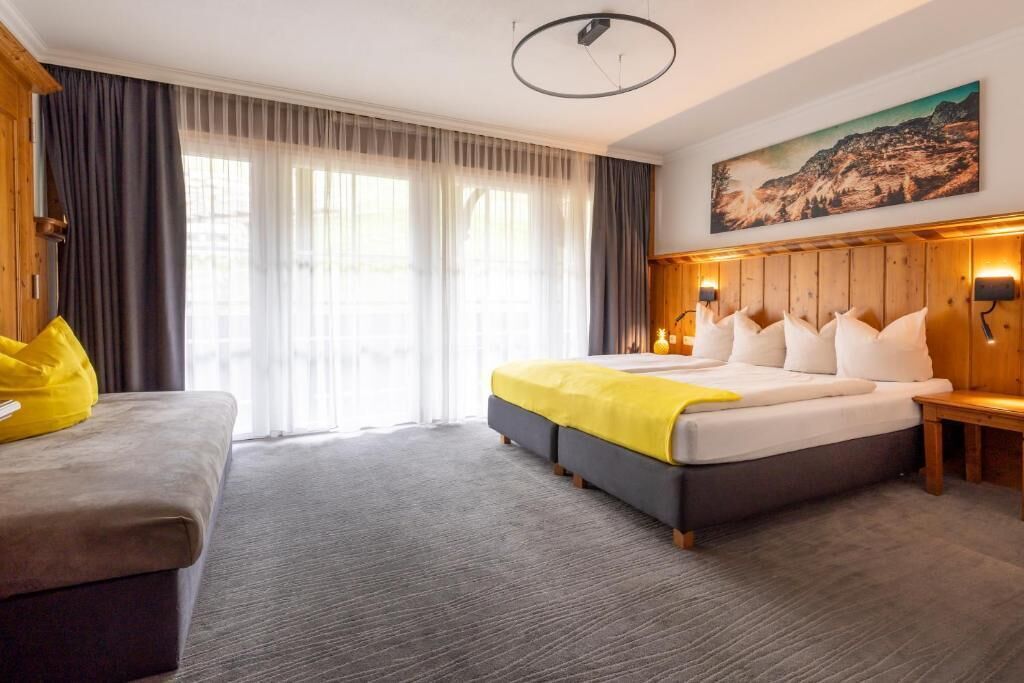 Une chambre d’hôtel avec un grand lit, un canapé, un tableau au mur et une fenêtre avec des rideaux.