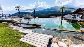 Piscina cristalina con terrazas de madera, sillas de descanso y vista a la montaña.
