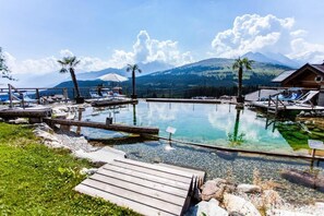 A clear pool with wooden decks, lounge chairs, and a mountain view.
