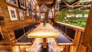 Un interior de madera con una larga mesa y bancos, cuadros en las paredes y una lámpara colgante.