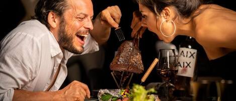Una mesa de comedor con un centro de carne asada, una botella de vino y una copa de vino tinto.