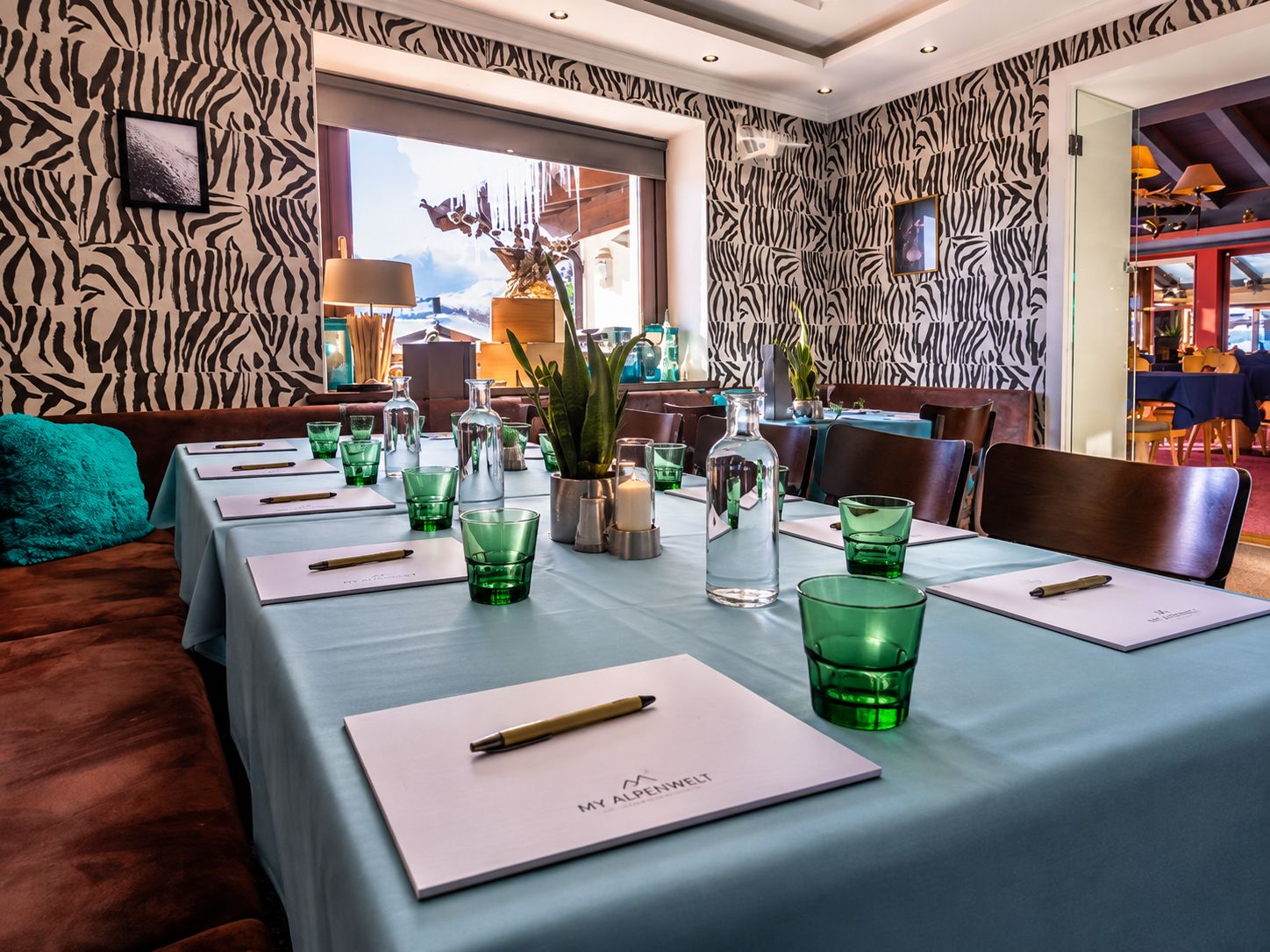 A dining area with zebra-patterned walls, tables set with green glassware, and a view of the cityscape through large windows.