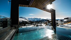 A modern indoor pool with a clear view of snow-covered mountains and a ski resort in the background. - MY ALPENWELT Resort – 4 Sterne Superior (Königsleiten)