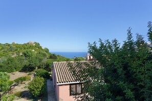 A coastal property with a terracotta roof, surrounded by lush greenery and overlooking the sea.