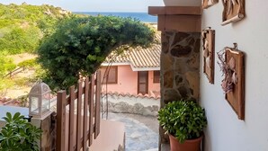 A balcony with a view of the sea, a wooden fence, potted plants, and wall-mounted decorations. - Costa Rei – Delightful Apartment with Garden (Muravera)