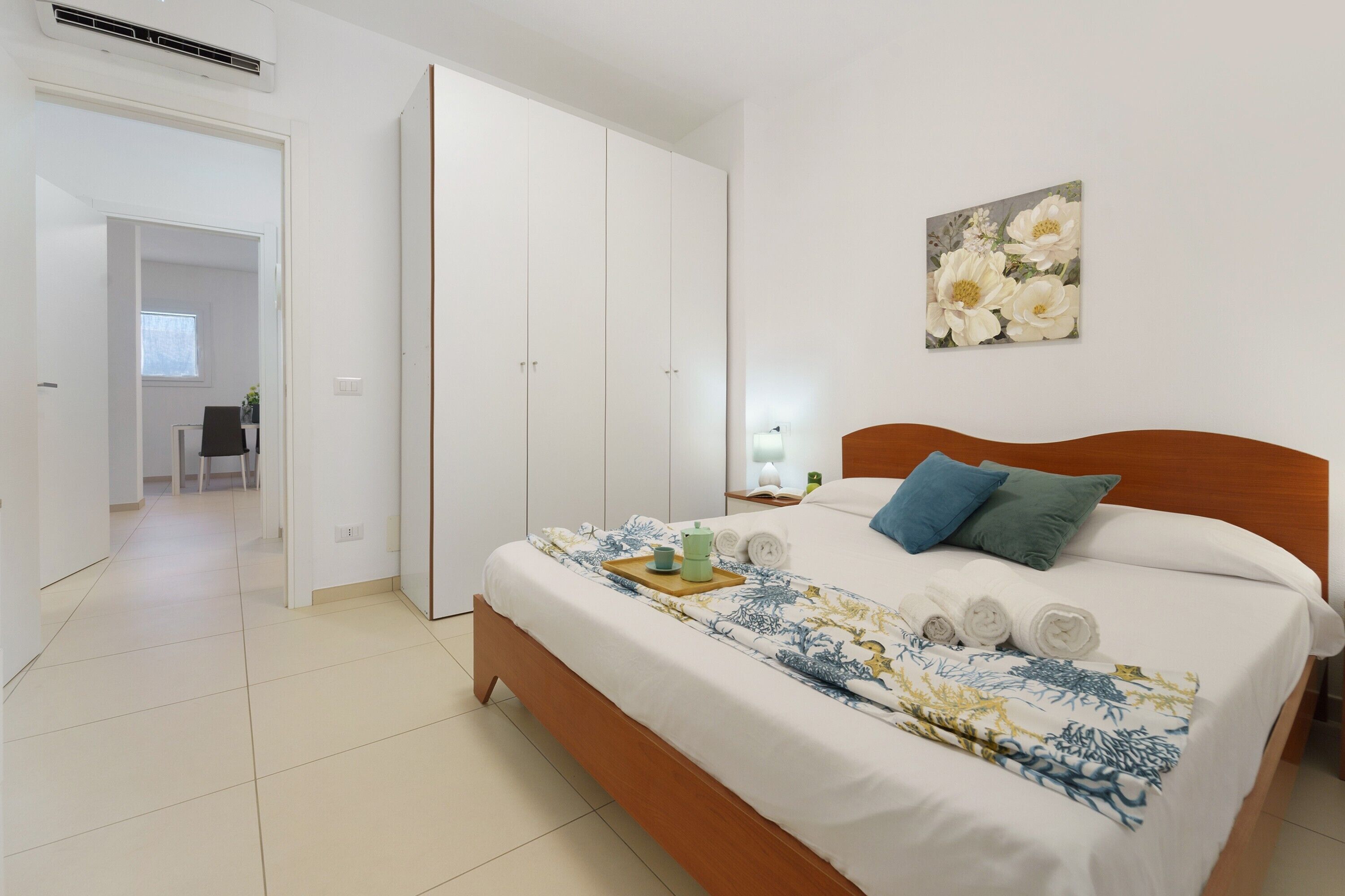 Un dormitorio con cama, mesita de noche, cuadro y puerta que da a otra habitación.