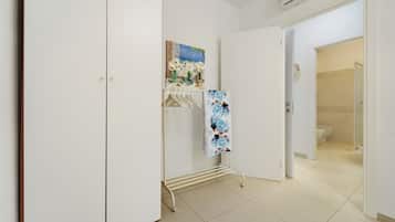 Ein Flur mit einem weißen Kleiderschrank, einem Kleiderständer mit Kleiderbügeln, einem Blumenbild und einem durchgegangenen Tür sichtbaren Badezimmer.