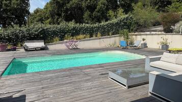 Eine Holzterrasse mit Schwimmbad, Gartenmöbeln und Blick auf Bäume.