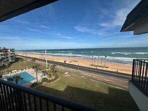 Blick vom Balkon auf einen Strand mit Pool, einer Straße und einem Gebäude im Hintergrund.
