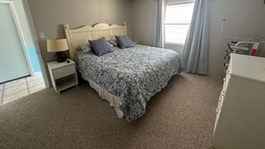 A bedroom with a bed, nightstand, lamp, and a window with curtains. - 2-Bedroom 2-Bathroom 5th "TOP" Floor Condo in Stunning Ormond Beach with AC (Ormond Beach)