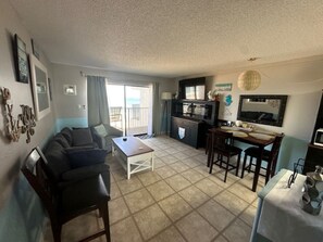 A living room with a sofa, a dining table, and a kitchen area. - Gorgeous Ocean & Pool View 5th "TOP" Floor 2/2 Condo in Beautiful Ormond Beach (Ormond Beach)