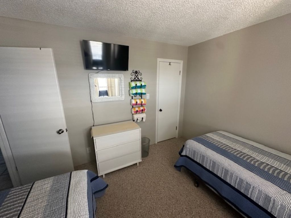 A bedroom with two beds, a dresser, a television mounted on the wall, and a window.