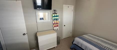 A bedroom with two beds, a dresser, a television mounted on the wall, and a window.