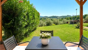 A covered outdoor seating area with a table and chairs, a potted plant, and a view of a green landscape. - Tenuta Gaetano Spadaro, Maurino Apartment (Capannori)