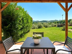 A covered outdoor seating area with a table and chairs, a potted plant, and a view of a green landscape. - Tenuta Gaetano Spadaro, Maurino Apartment (Capannori)