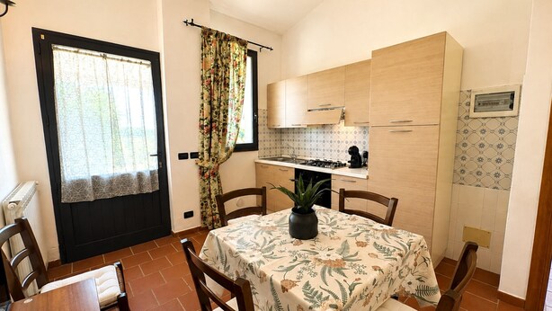 A compact kitchen with a dining area, a potted plant on the table, and a window with curtains. - Tenuta Gaetano Spadaro, Maurino Apartment (Capannori)