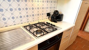 A kitchen with a gas stove, oven, and a coffee maker on the countertop. - Tenuta Gaetano Spadaro, Maurino Apartment (Capannori)