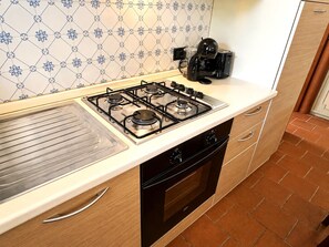 A kitchen with a gas stove, oven, and a coffee maker on the countertop. - Tenuta Gaetano Spadaro, Maurino Apartment (Capannori)