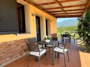 An outdoor patio with a table and chairs, a brick wall, and a view of the mountains. - Tenuta Gaetano Spadaro, Maurino Apartment (Capannori)